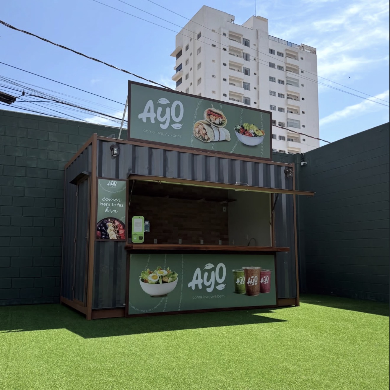 Contêiner verde da Ayo visto de lado, com o toldo aberto e o gramado na frente