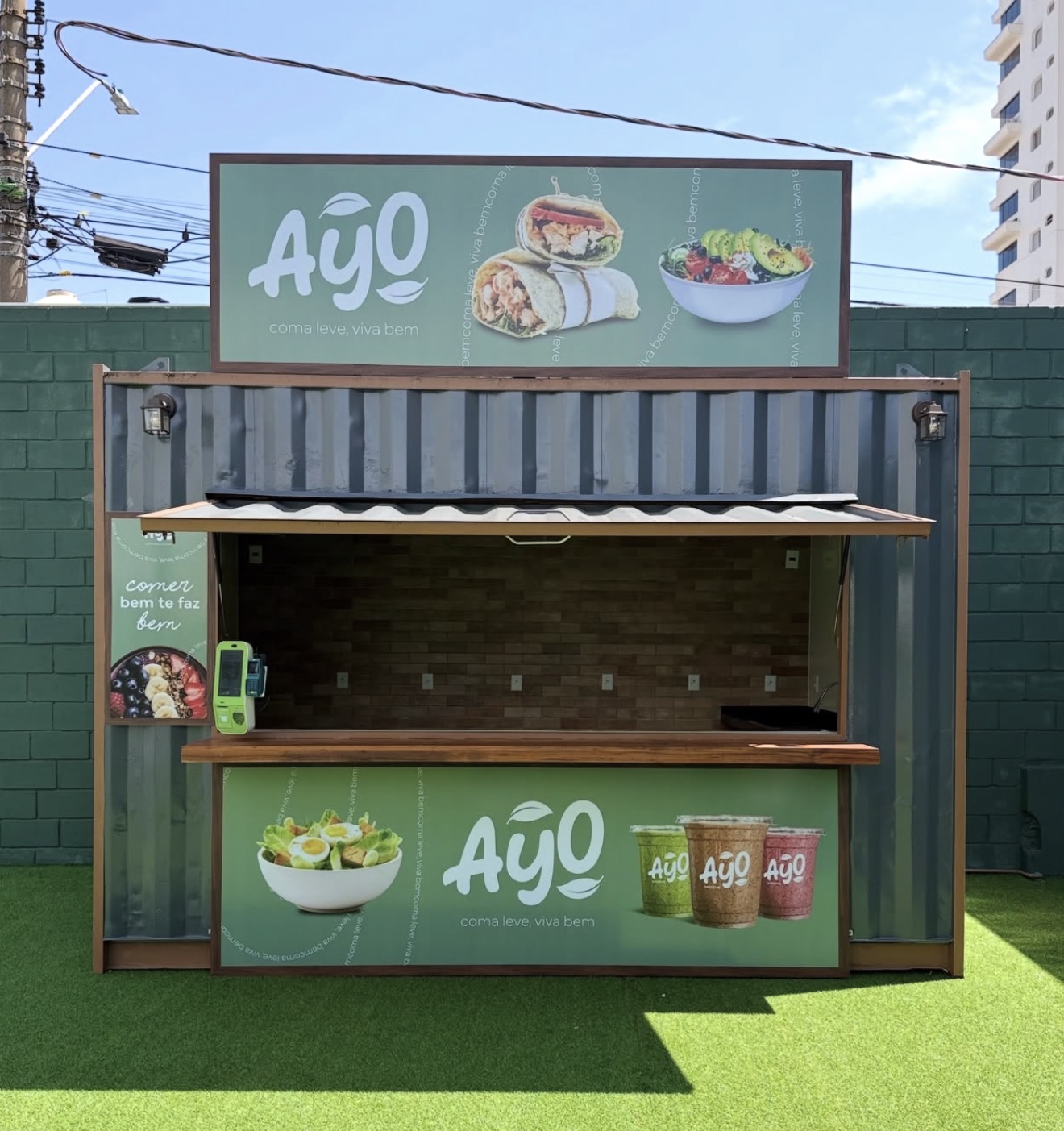 Frente do contêiner da Ayo com o balcão de madeira e as placas com wraps, saladas e sucos